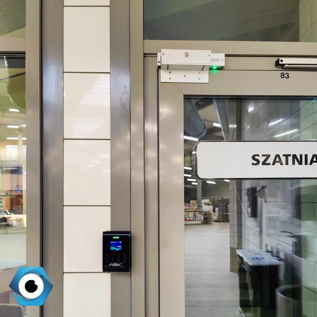 Elegancki czytnik systemu RCP i kontroli dostępu zamontowany na framudze przy szklanych drzwiach wejściowych do biura.