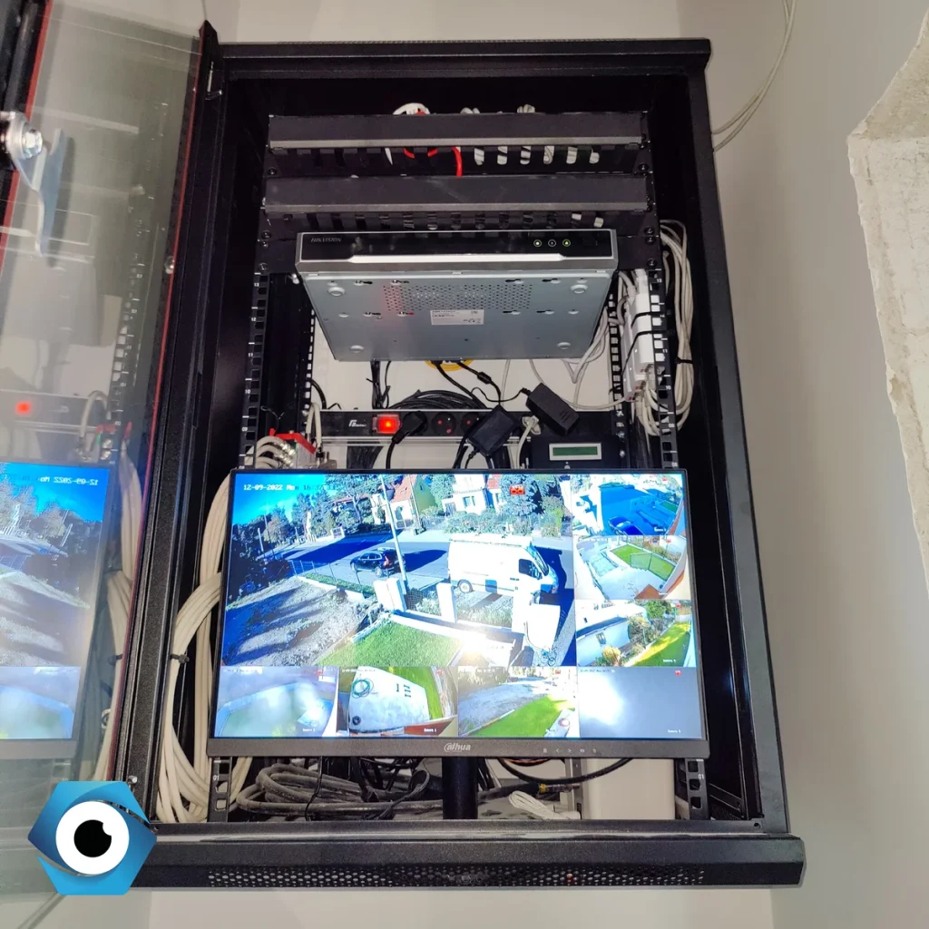 Instalacje teletechniczne wewnątrz szafy RACK zawierające profesjonalny rejestrator monitoringu Hikvision, uporządkowane okablowanie oraz monitor Dahua wyświetlający obraz z kamer CCTV na żywo.