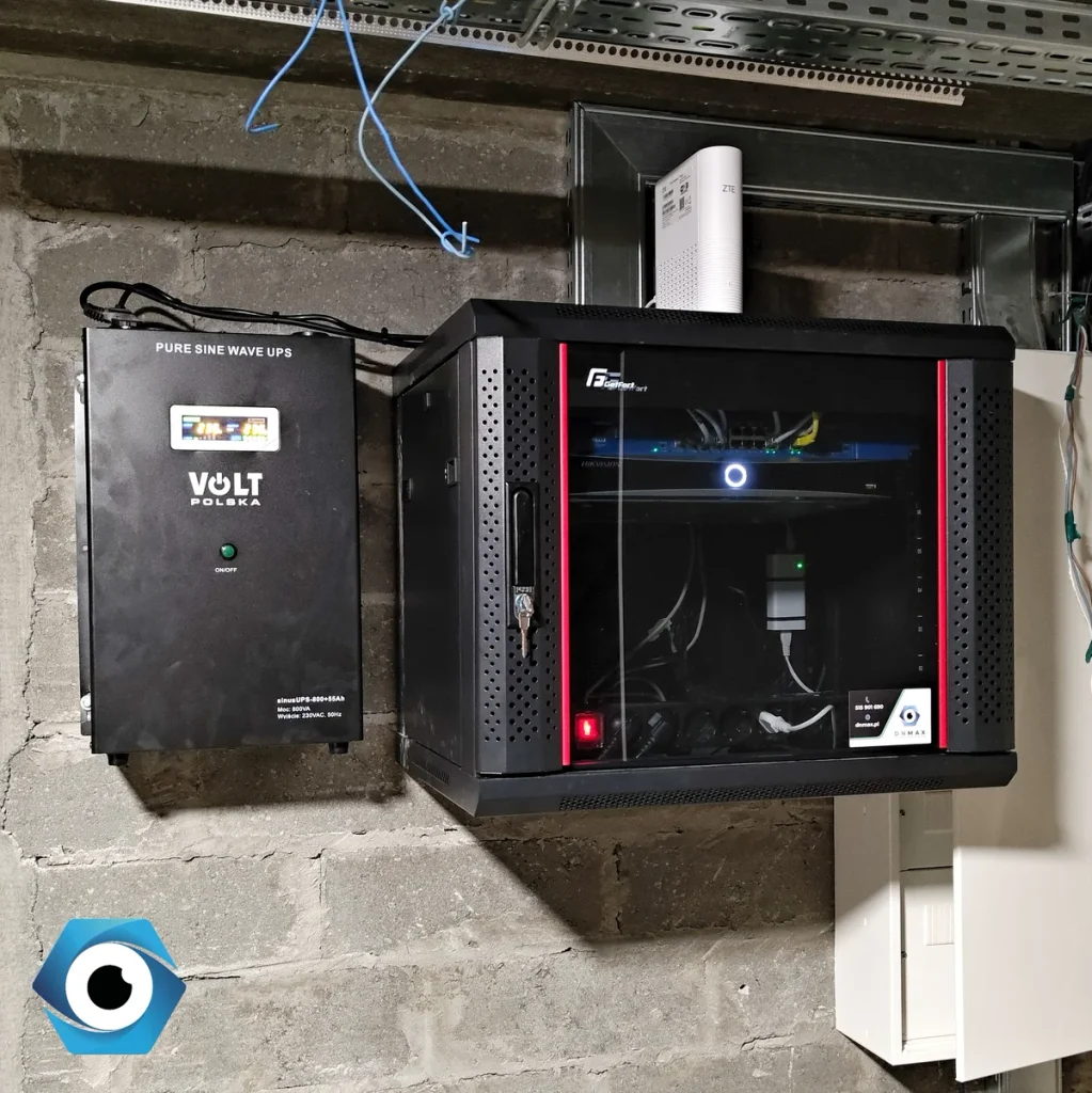 Domowa szafa RACK ze szklanymi drzwiami mieszcząca instalację sieciową i sprzęt Hikvision, połączona z zewnętrznym zasilaczem awaryjnym UPS Volt Polska gwarantującym podtrzymanie zasilania systemu.